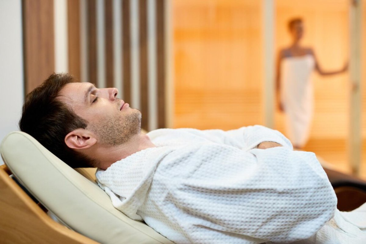 Man relaxing in a reclining chair at a spa, with a woman in the background.