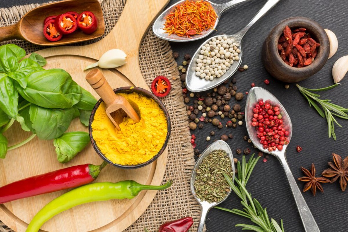 Assorted spices and herbs displayed on spoons and bowls on a dark surface.