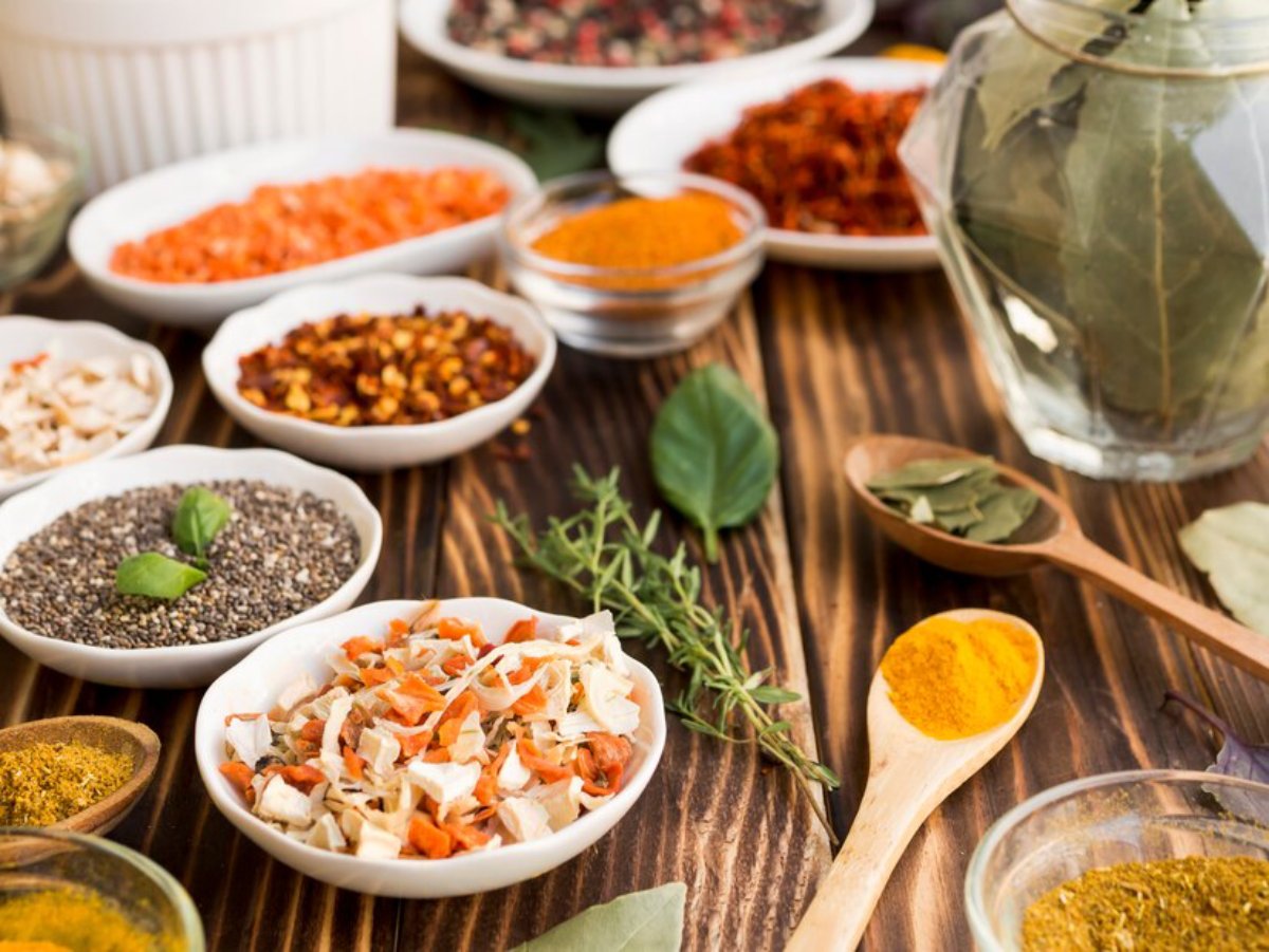Assortment of spices and herbs in various bowls and spoons on a wooden table.