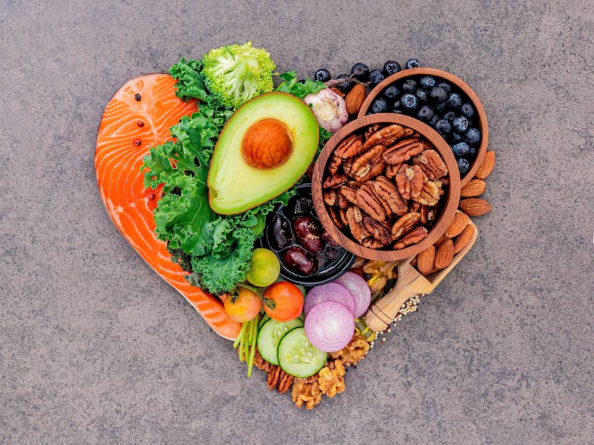 A heart-shaped array of healthy foods, featuring salmon, avocado, nuts, and various fresh vegetables and fruits.