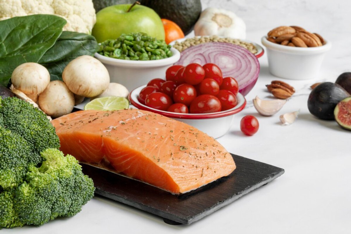 Assorted healthy foods including salmon, vegetables, fruits, and nuts on a white marble surface.