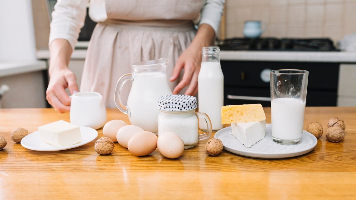 A person prepares food using various dairy products like milk, cheese, and eggs on a kitchen counter.
