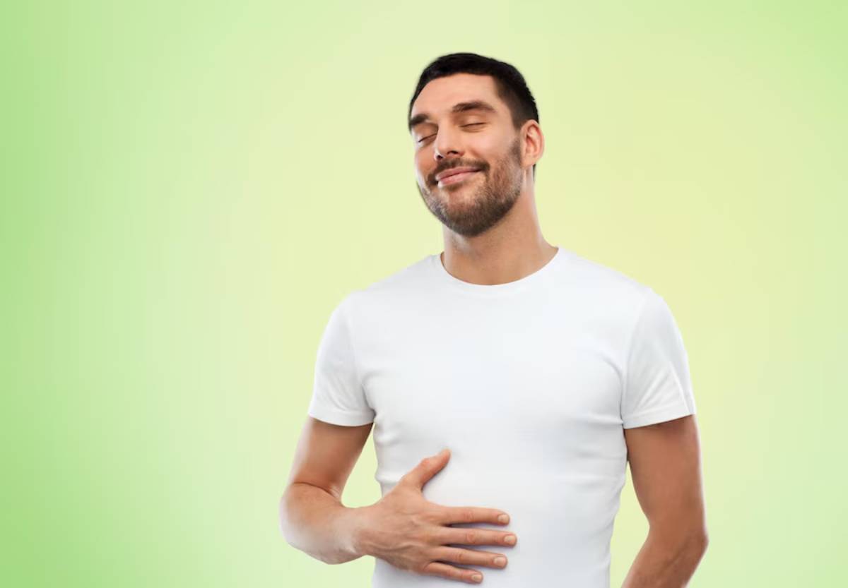 Man in a white t-shirt, smiling contentedly with eyes closed, hand on his chest, against a soft green background.