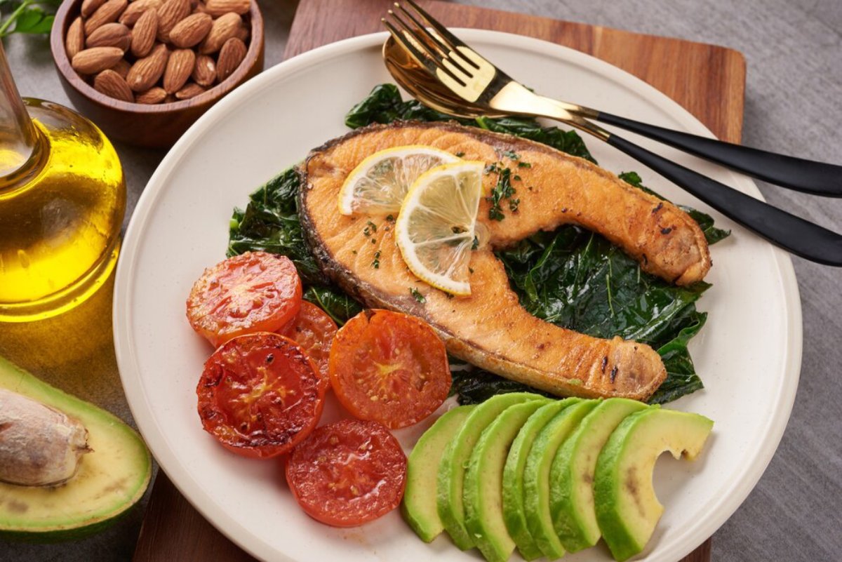 Grilled salmon on a bed of spinach with sliced avocado, roasted tomatoes, almonds, and olive oil on the side.