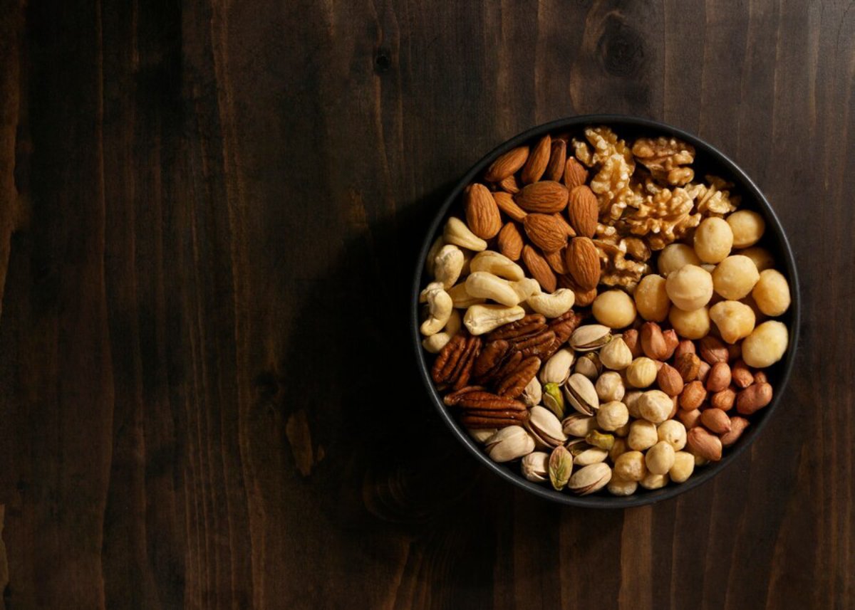 A bowl of mixed nuts including almonds, walnuts, and cashews on a dark wooden table.