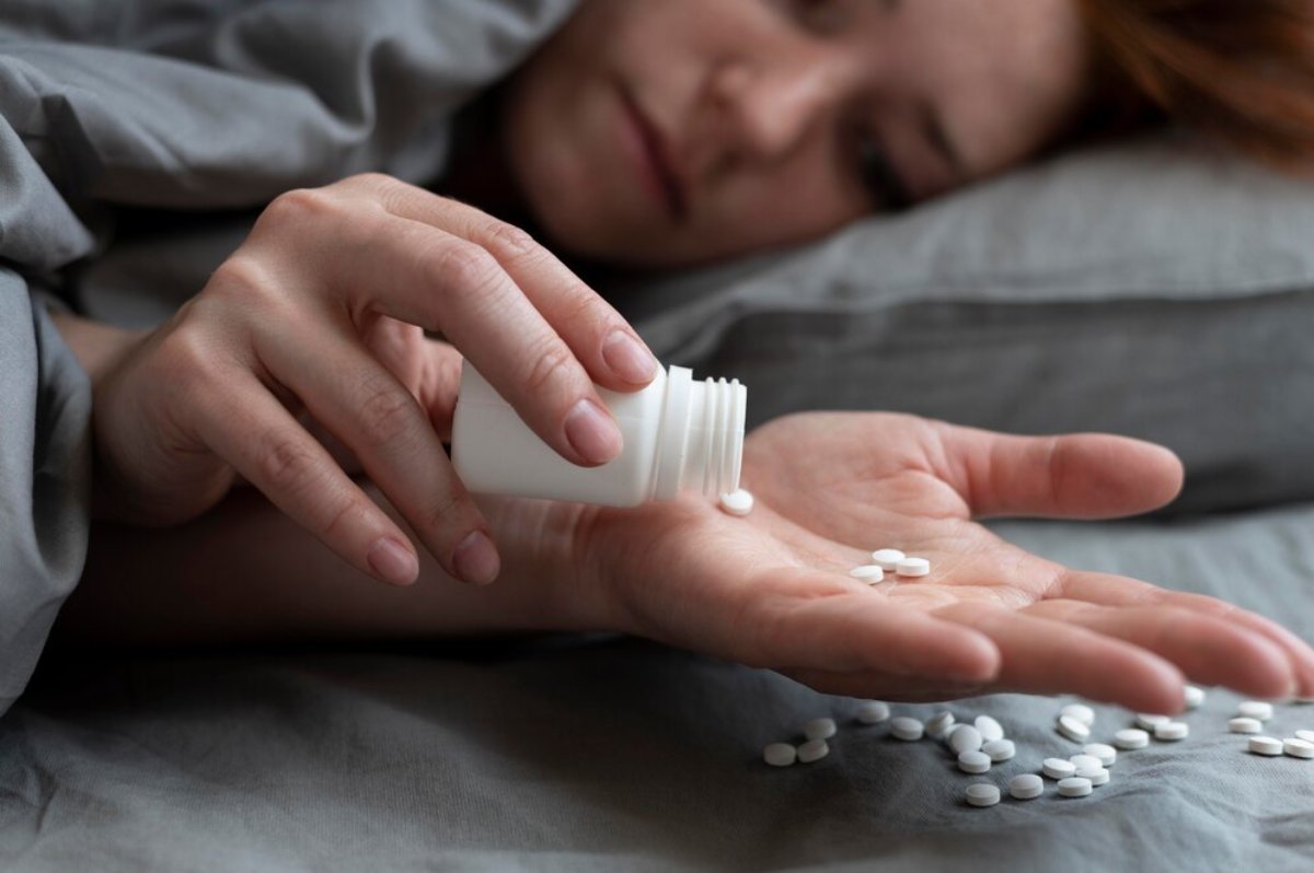 Woman lying in bed, pouring pills from a bottle into her hand, looking distressed.