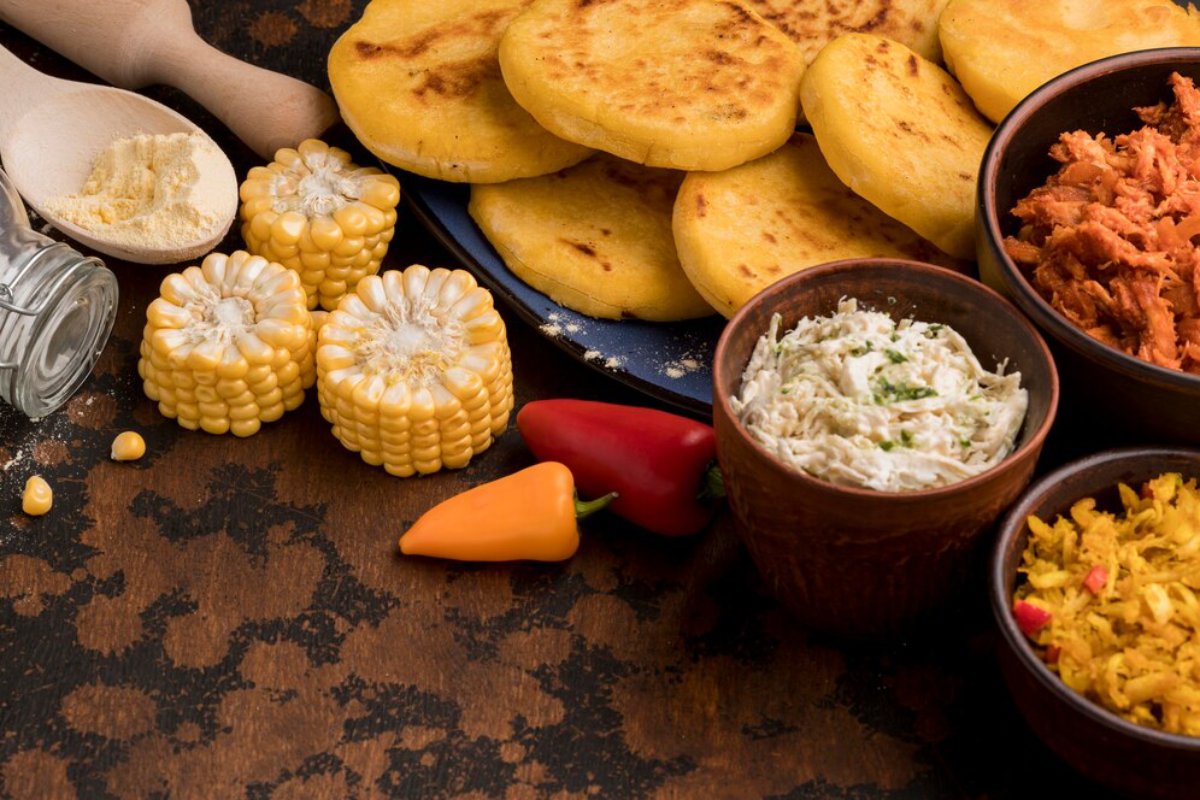 Assorted traditional South American dishes including arepas, corn, and various small bowls of toppings and sides on a rustic table.