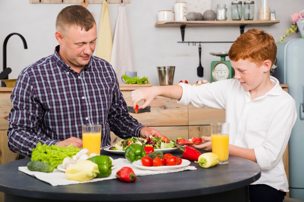 Father and son enjoying preparing a healthy salad together in the kitchen.