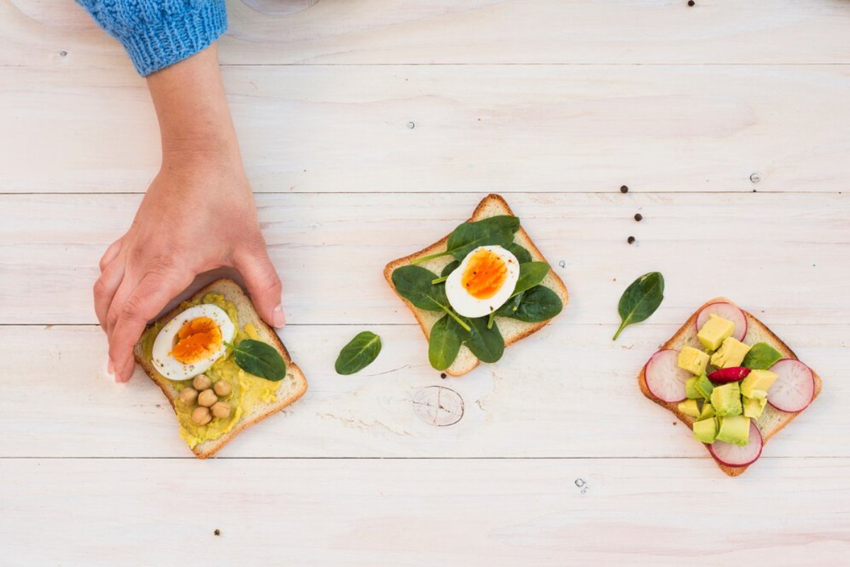A person arranging three open sandwiches with various toppings on a wooden table.