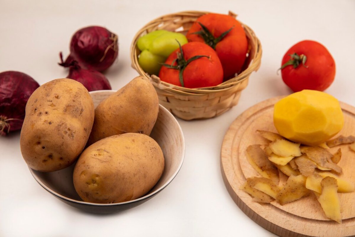 A variety of vegetables including potatoes, beets, tomatoes, and a peeled lemon on a white surface.