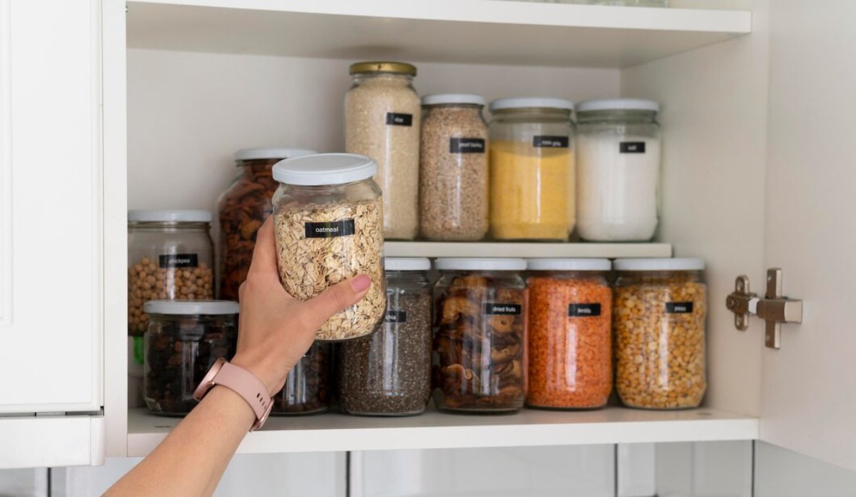 Person organizing labeled jars of dry goods like oatmeal and beans in a pantry cabinet.