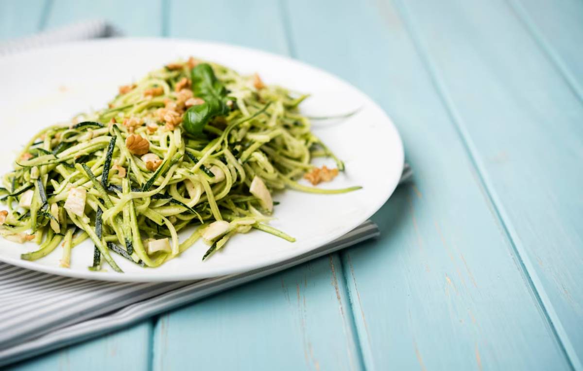 Plate of zucchini noodles with spinach and nuts on a teal wooden table.