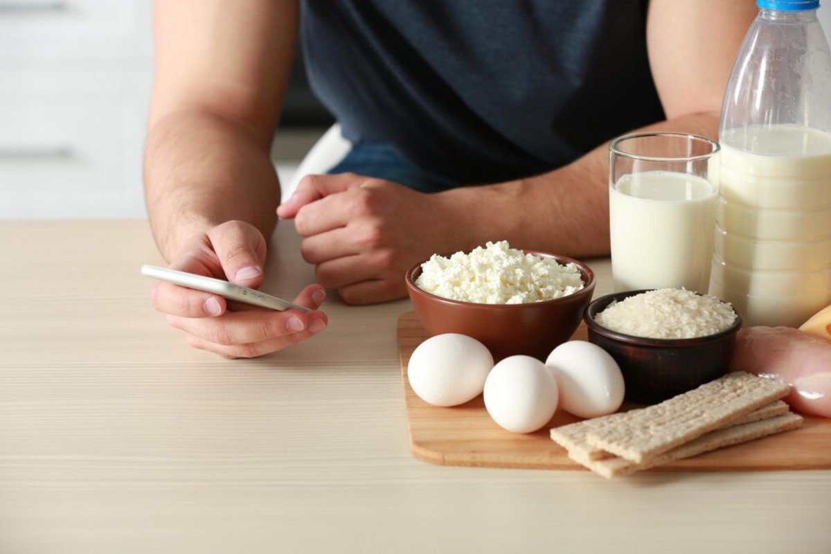 A person using a smartphone at a table with various dairy products and eggs.