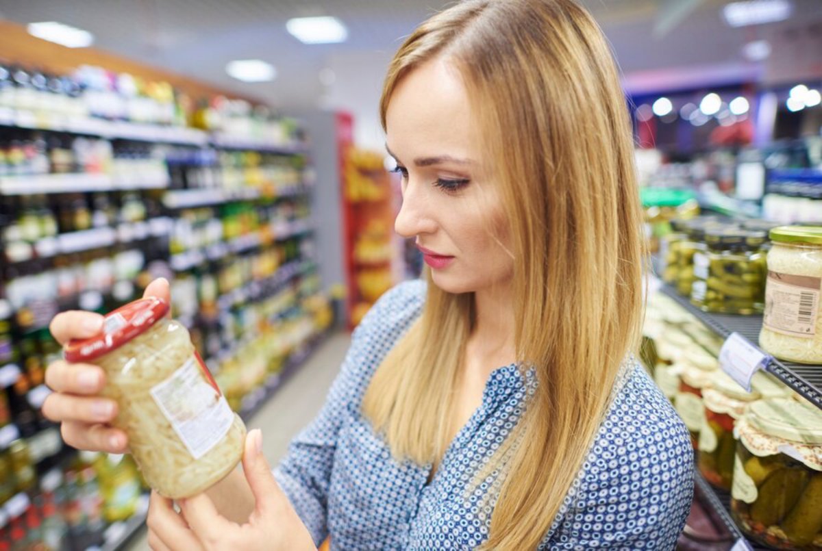 Woman examines a jar of food in the grocery store aisle.