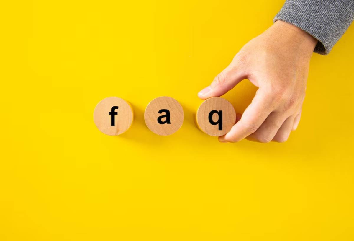 A hand arranging round wooden blocks spelling FAQ on a yellow background.