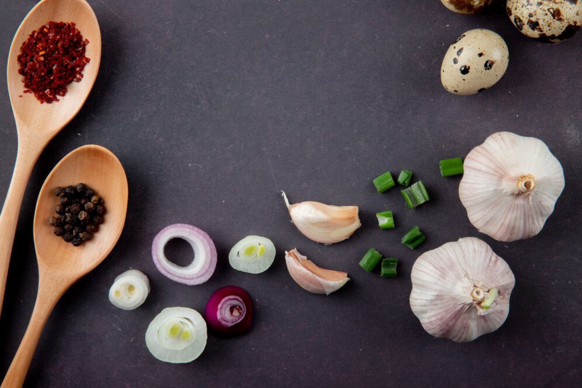 Assorted spices and ingredients including garlic, onions, and quail eggs displayed on a dark surface.