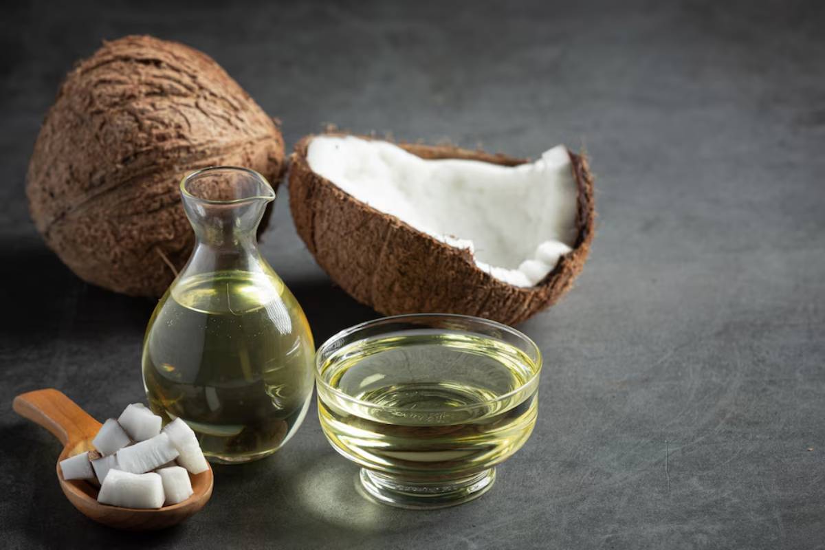 Whole and halved coconuts with coconut oil in a glass jar and bowl on a dark surface.