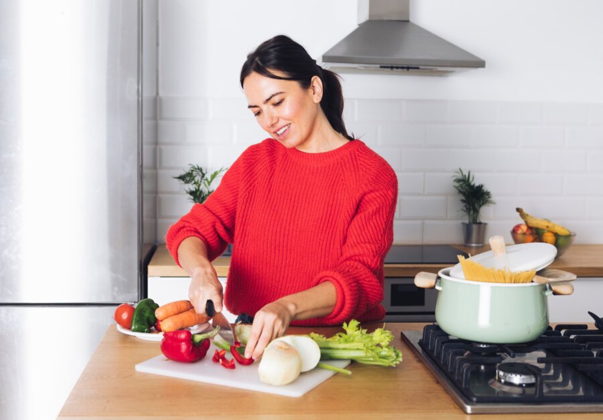 A person in a red sweater chops vegetables, including bell peppers and carrots, on a countertop in a modern kitchen.