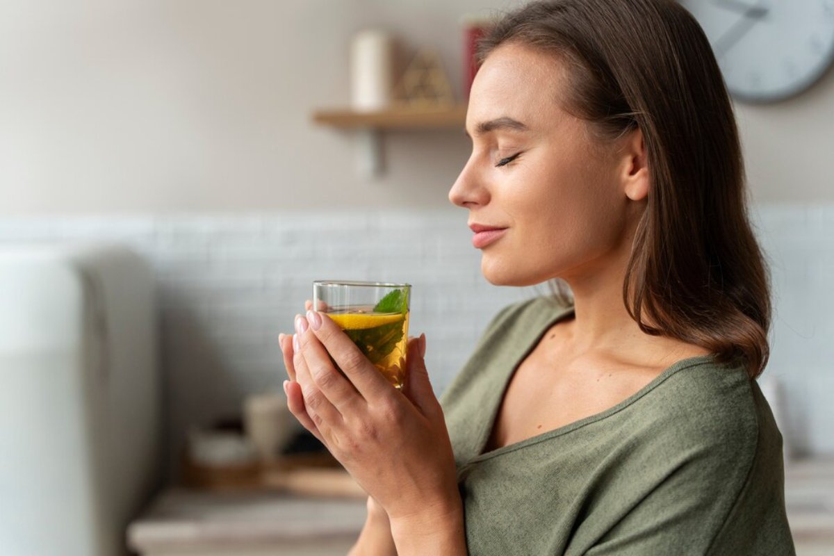Woman in a green top enjoying a soothing moment with a cup of lemon tea in a cozy kitchen.