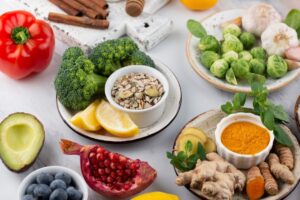 Assorted fresh vegetables, fruits, seeds, and spices arranged on a white table.