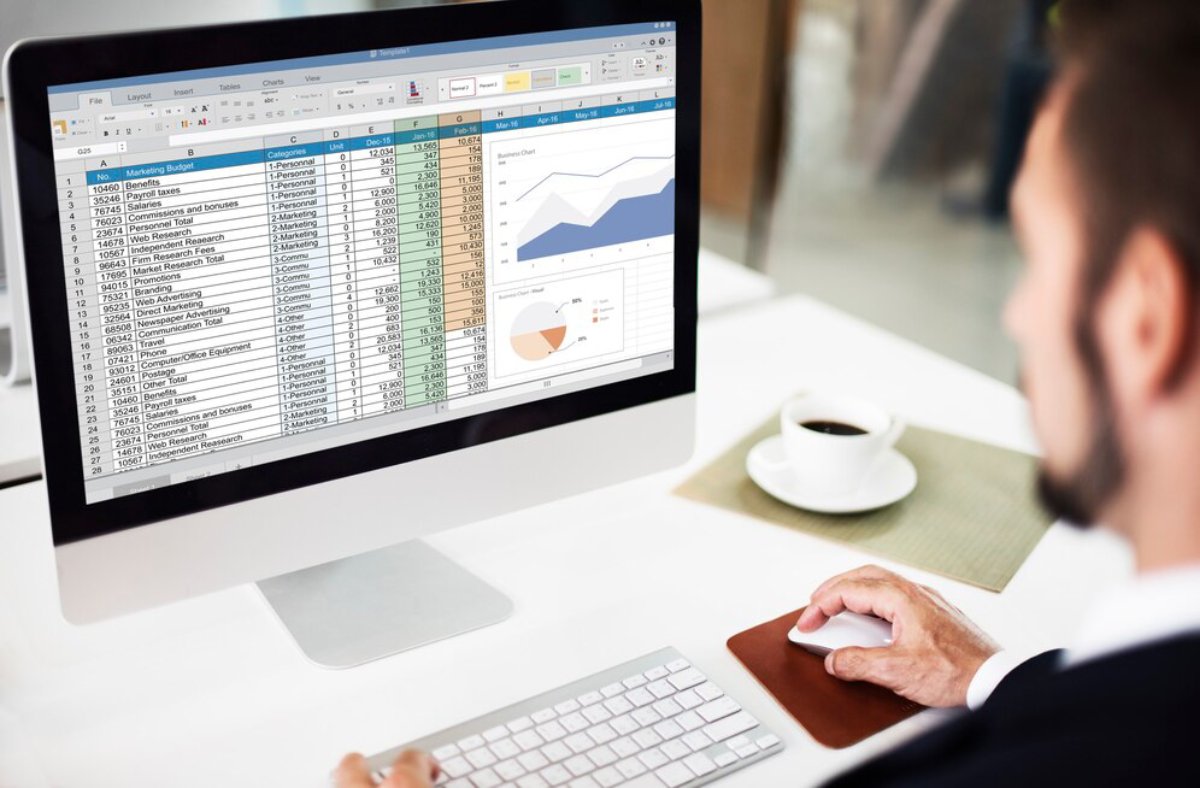 Man reviewing detailed spreadsheets and charts on a computer screen in an office setting.