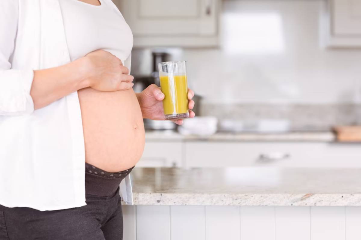 Pregnant woman in a kitchen, holding a glass of orange juice.