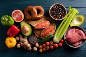 Assorted healthy foods including fruits, vegetables, nuts, beans, and raw meats on a dark wooden table.