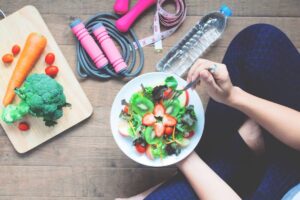 Overhead view of a person eating a colorful salad, with fitness gear and vegetables laid out on a wooden surface.