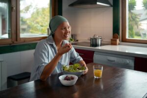 A woman in a turban smiling while eating a salad in a cozy kitchen.