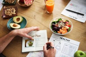 Person planning a healthy diet with fresh food, a diet plan booklet, and health charts on a wooden table.