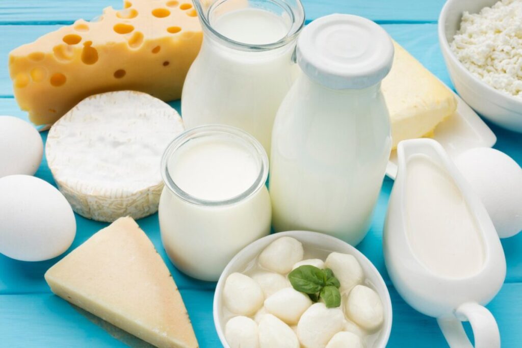 Assortment of dairy products including cheese, milk, and eggs on a blue wooden table.