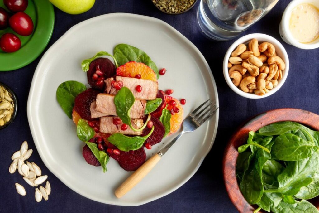 A healthy meal of sliced beets, oranges, spinach, and turkey slices garnished with pomegranate on a white plate.