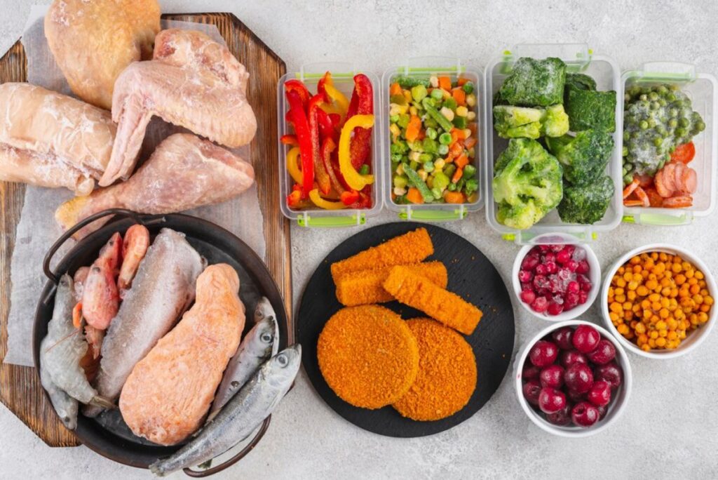 Assorted raw meats and breaded cutlets with containers of colorful vegetables and frozen berries, displayed for meal preparation.