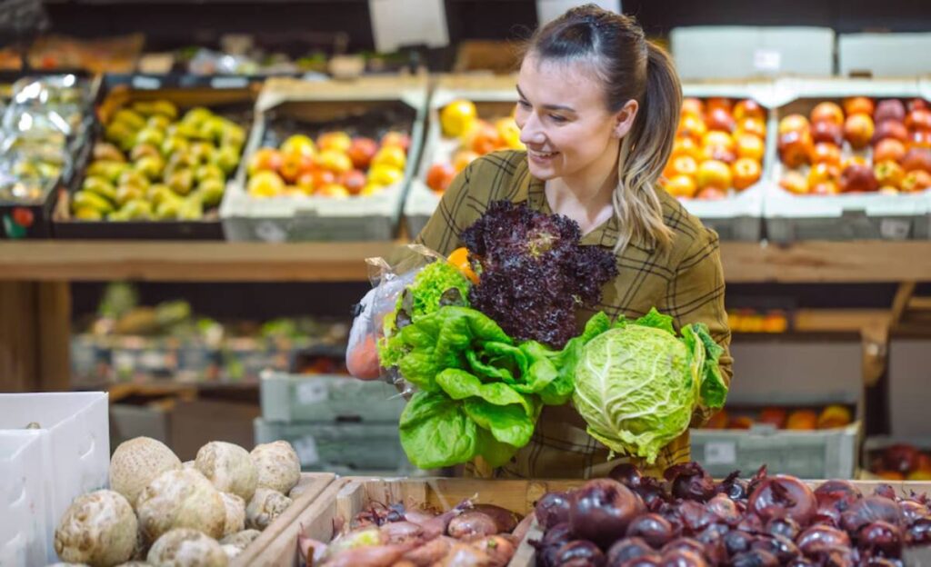 Woman smiling and holding fresh vegetables in a grocery store.