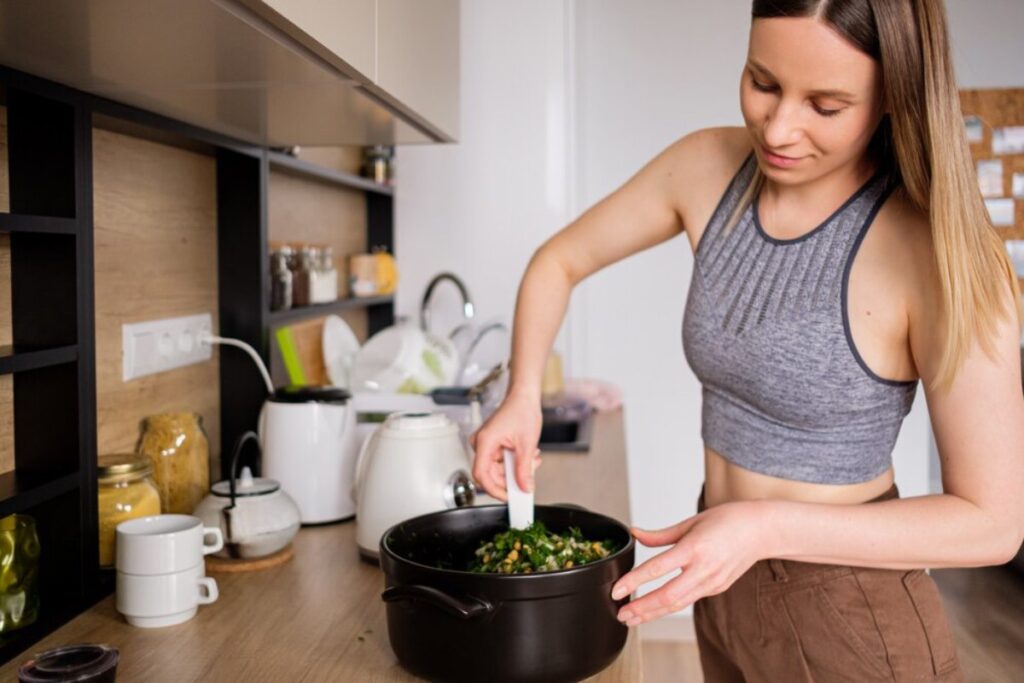 Young woman cooking spinach in a pot in a modern kitchen.
