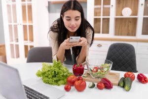 Woman using smartphone while preparing salad with various vegetables in a modern kitchen.