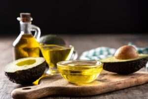 Avocado halves and avocado oil in glass containers on a wooden table.