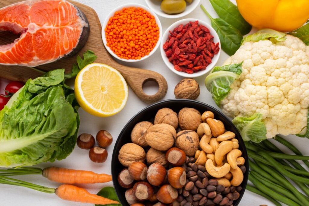 A vibrant assortment of fresh vegetables, fruits, nuts, and salmon, highlighting a healthy, colorful spread on a white background.