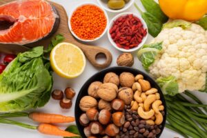 A vibrant assortment of fresh vegetables, fruits, nuts, and salmon, highlighting a healthy, colorful spread on a white background.